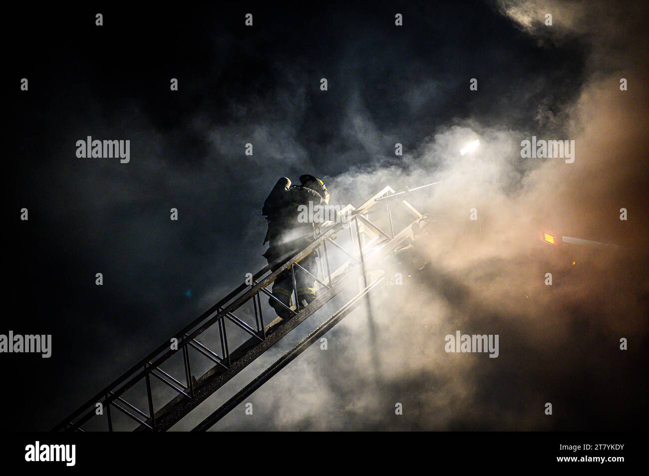 Un pompiere si arrampica su una lunga scala da un camion in azione per combattere uno spettacolare blaise presso il legname RK Miles a Montpelier, VT, New England, USA. Foto Stock