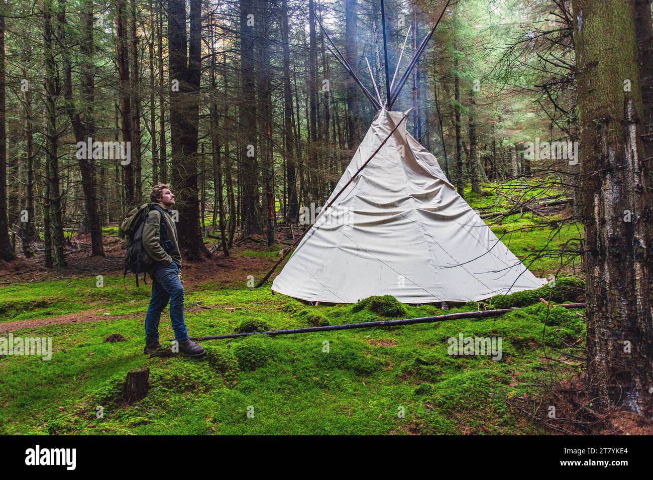 Uomo con zaino in piedi accanto alla tenda tipi in mezzo alla natura e al paesaggio forestale Foto Stock