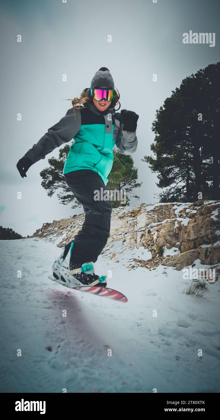 Uno snowboarder che indossa attrezzatura per sport invernali sta scendendo su una collina innevata mentre si afferra un bastone da sci in entrambe le mani Foto Stock