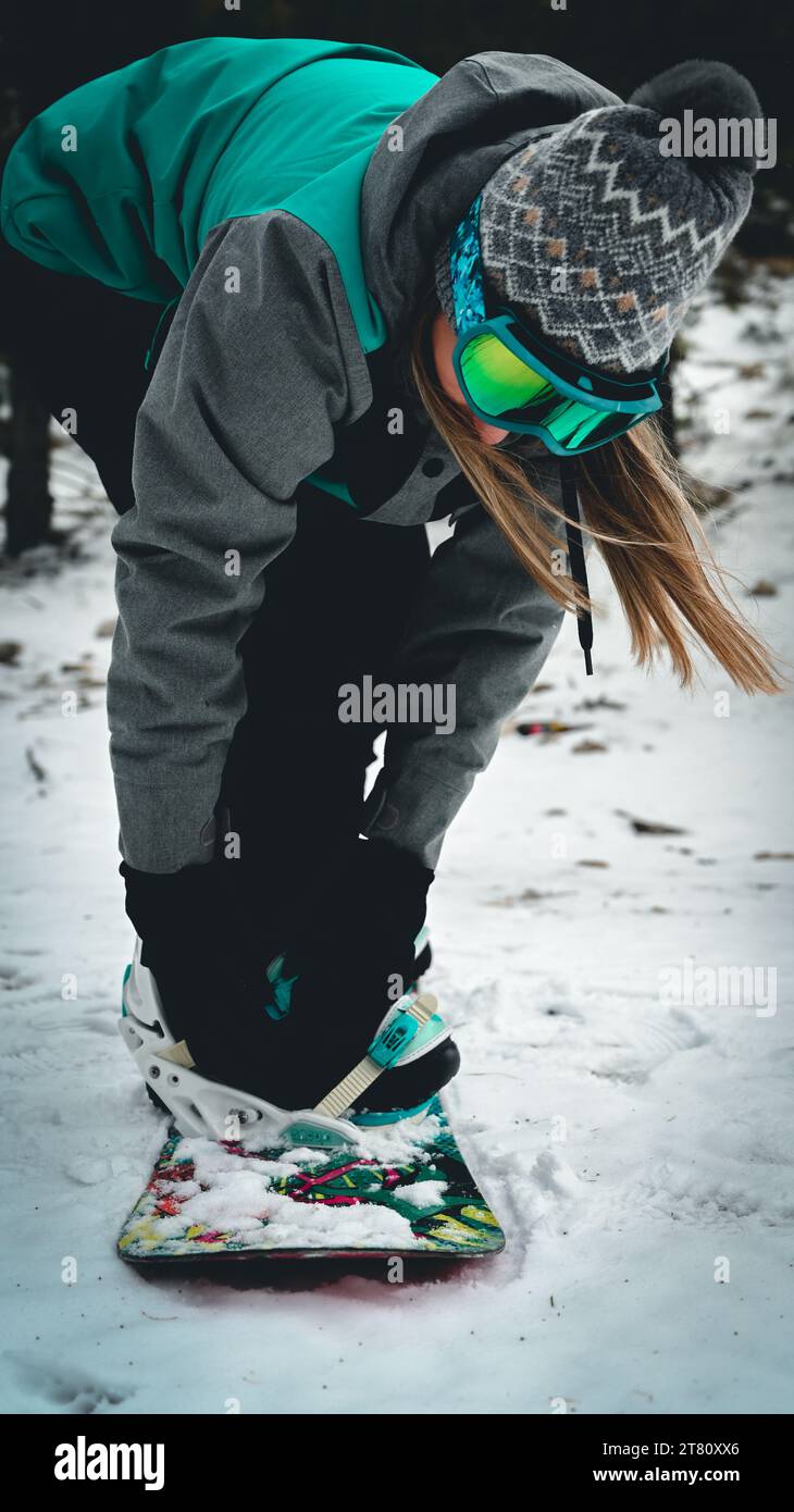 Una snowboarder donna con equipaggiamento invernale completo che si inclina in avanti sullo sfondo innevato del paesaggio invernale, pronta a iniziare la sua discesa lungo la pista Foto Stock