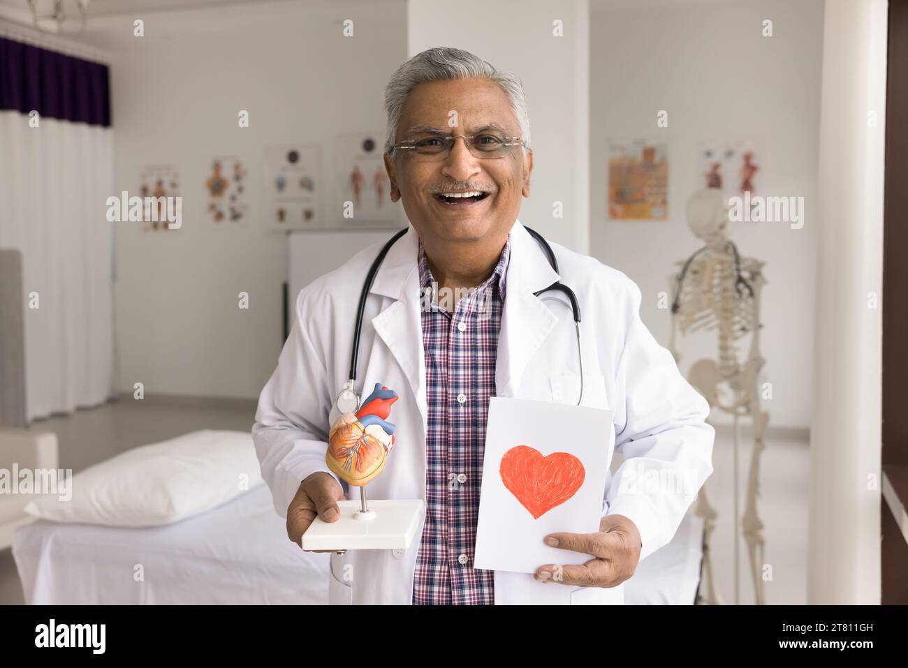 Allegro vecchio medico cardiologo indiano in posa in ufficio ospedaliero Foto Stock