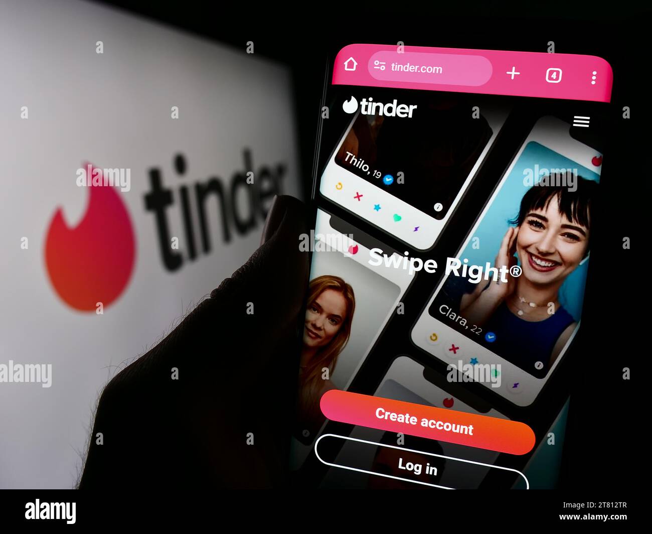 Persona che possiede un cellulare con una pagina Web dell'app di incontri online degli Stati Uniti Tinder davanti al logo dell'azienda. Concentrarsi sul centro del display del telefono. Foto Stock