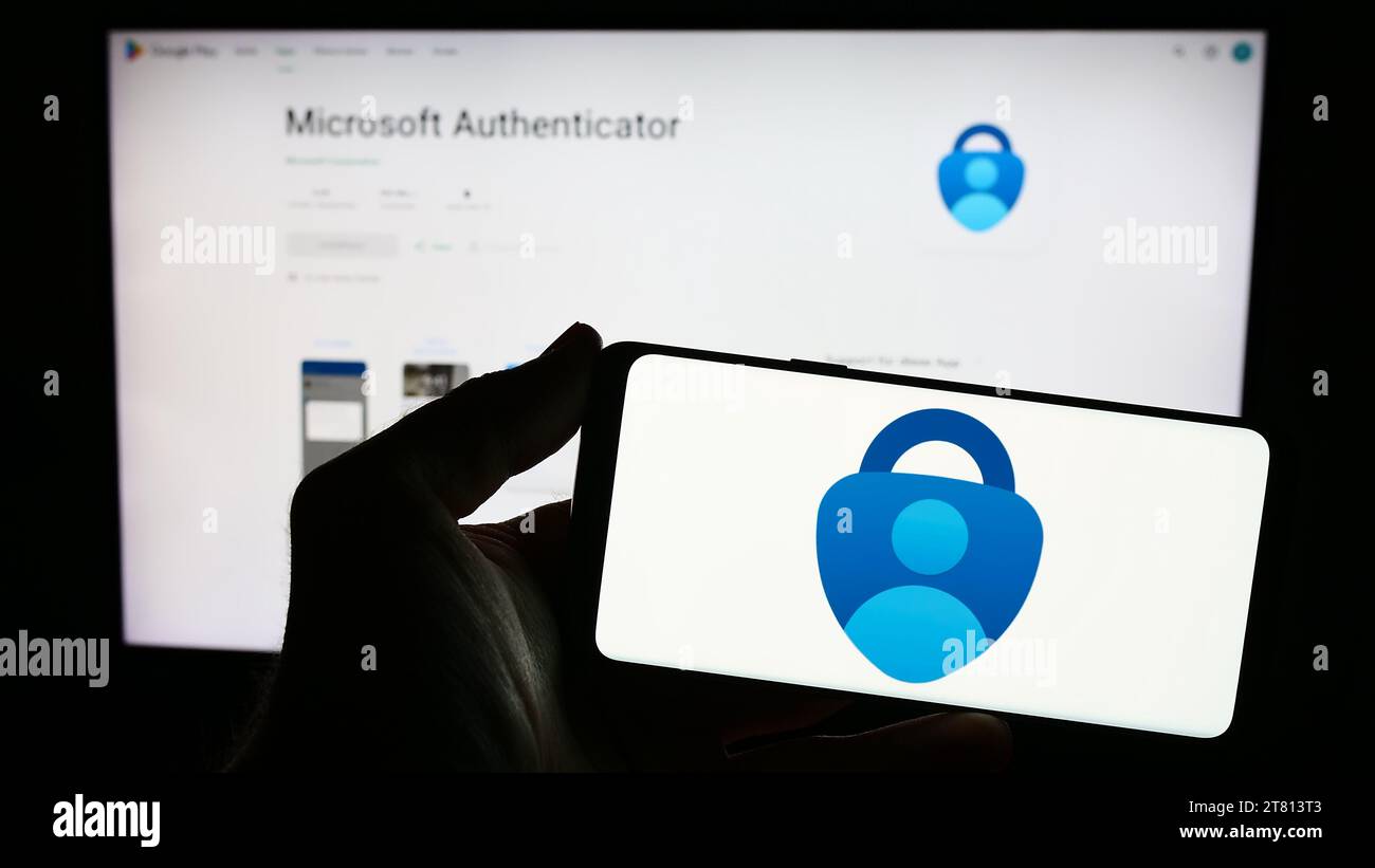 Persona che possiede uno smartphone con il logo dell'app di autenticazione Microsoft Authenticator davanti al sito Web. Concentrarsi sul display del telefono. Foto Stock