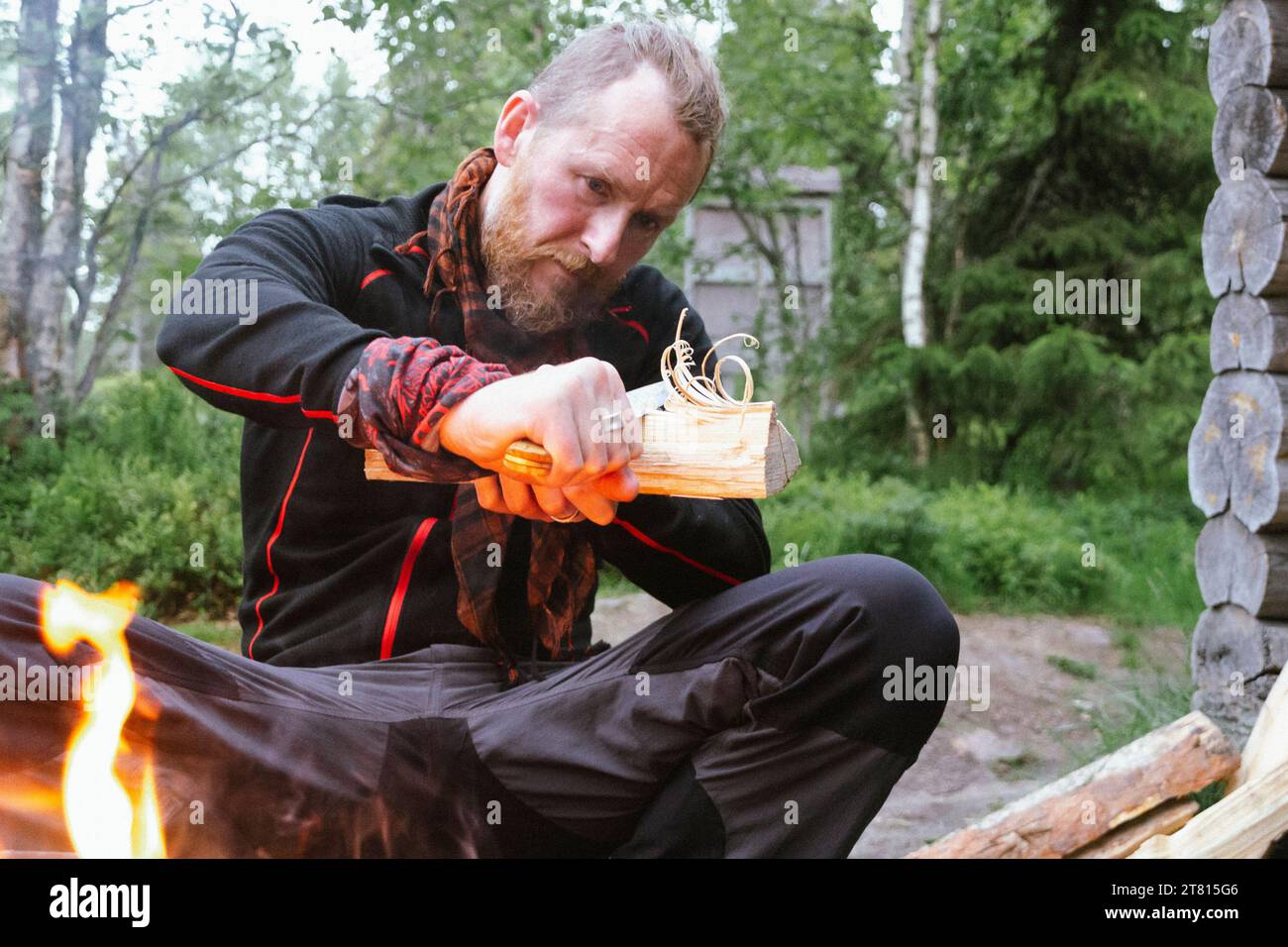 Un uomo scolpisce bastoncini di piume in un pezzo di legno per accendere un incendio nella foresta su un sentiero escursionistico nel nord della Finlandia Foto Stock