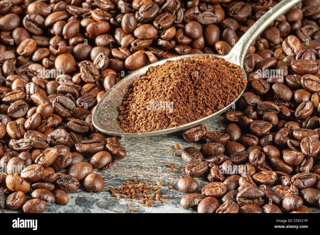 Tema del caffè. Un cucchiaio riempito di caffè macinato si trova tra una pila di chicchi di caffè. Foto Stock