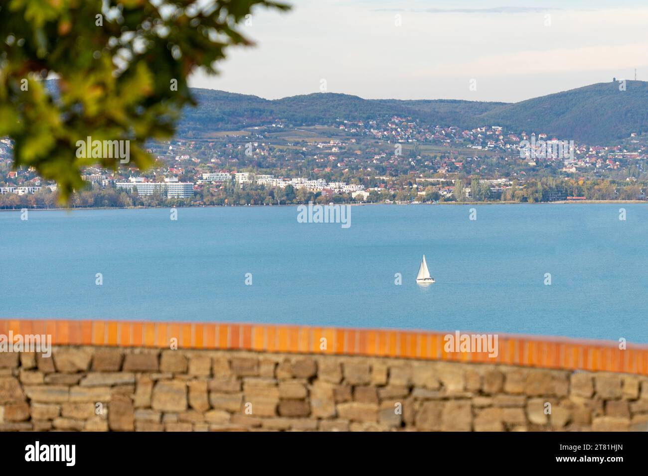 Una nave a vela sul lago Balaton alla luce del sole autunnale con Balatonfüred sullo sfondo Foto Stock