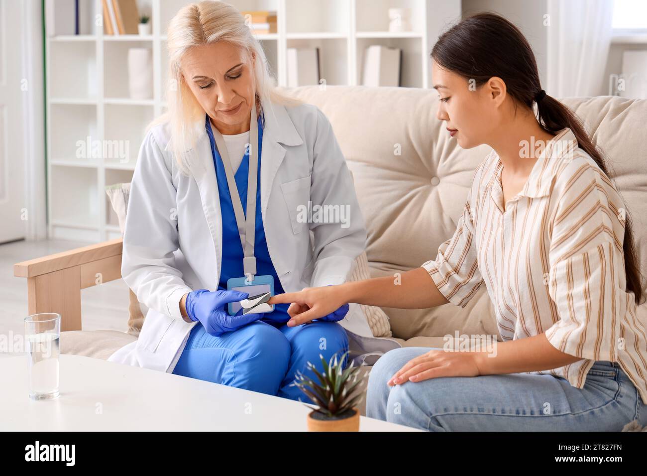 Medico femminile che prende il polso dal paziente a casa Foto Stock