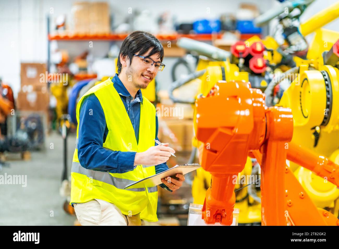 Giovane ingegnere giapponese responsabile del controllo di una linea di produzione industriale di bracci robotici Foto Stock