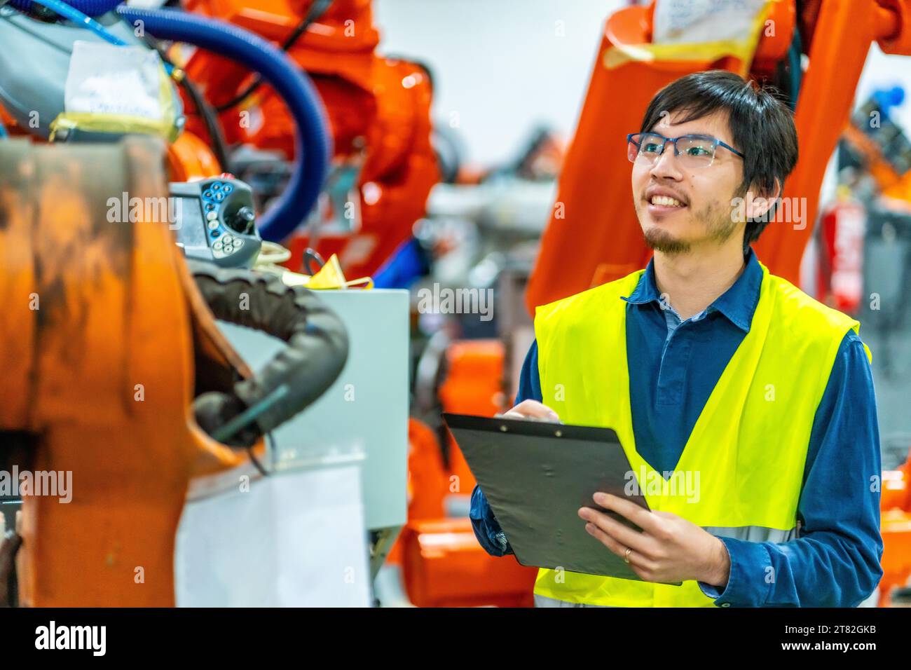 Vista laterale di un orgoglioso ingegnere giapponese in un'industria di robot industriali Foto Stock
