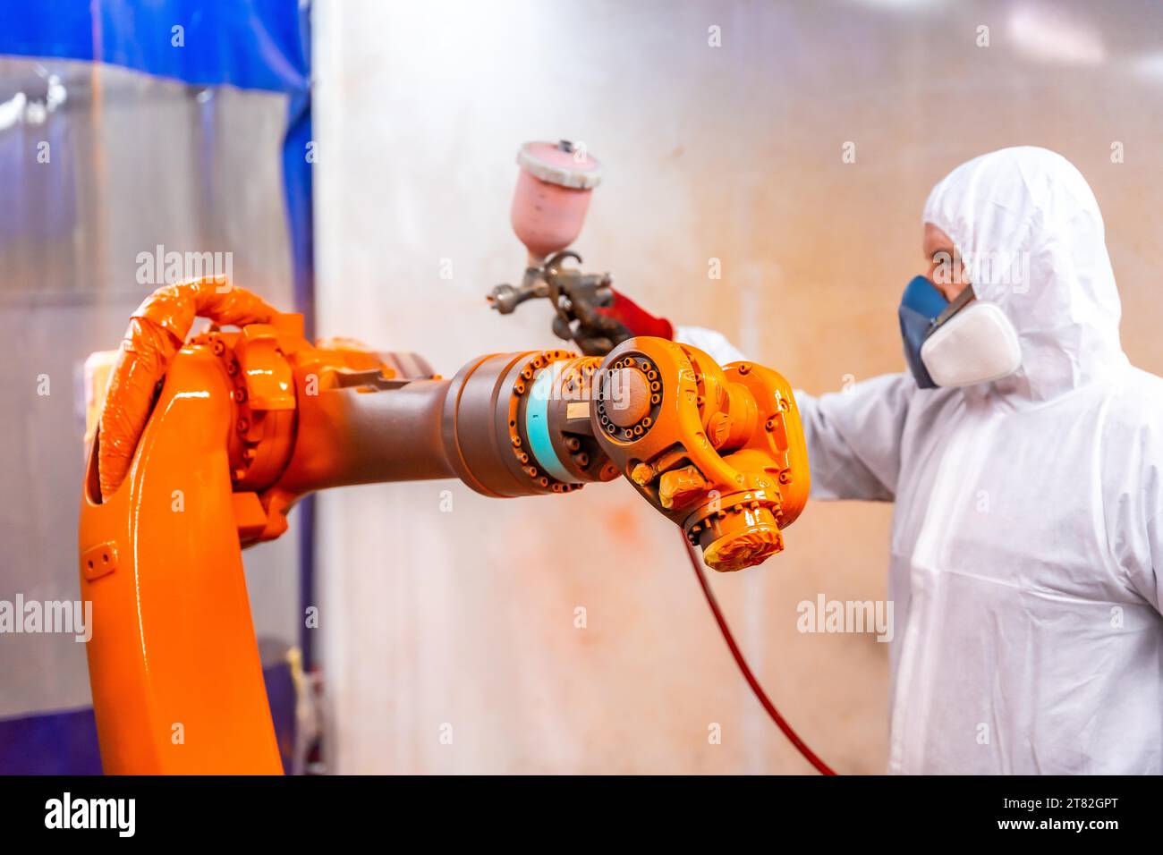 Pittore industriale che dipinge un braccio robotizzato con spray in un'industria robotica industriale Foto Stock