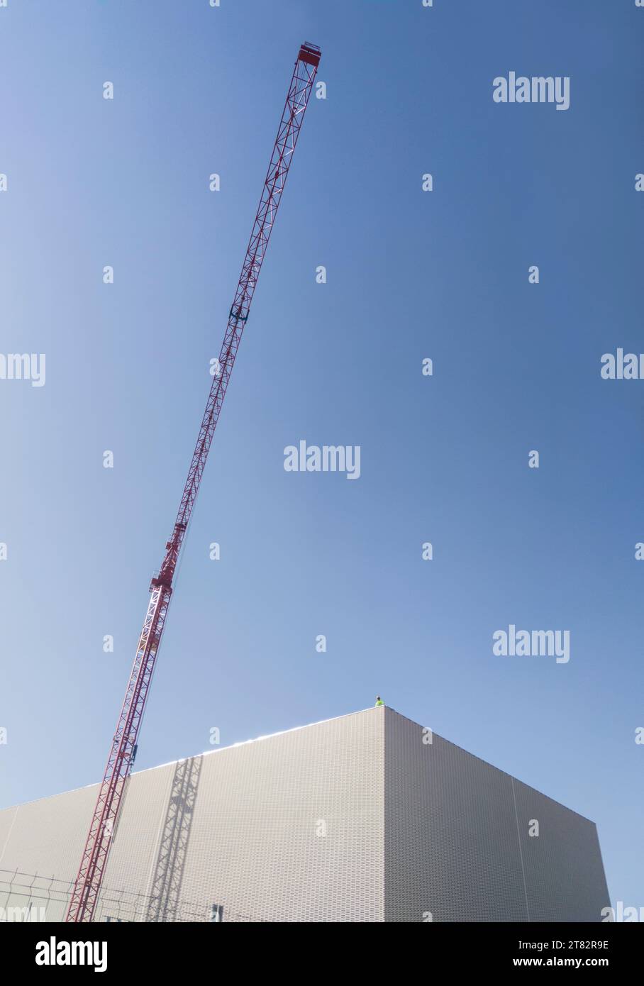 Lavoratore in cima a un edificio in costruzione con gru rossa. Cielo nuvoloso blu sullo sfondo Foto Stock