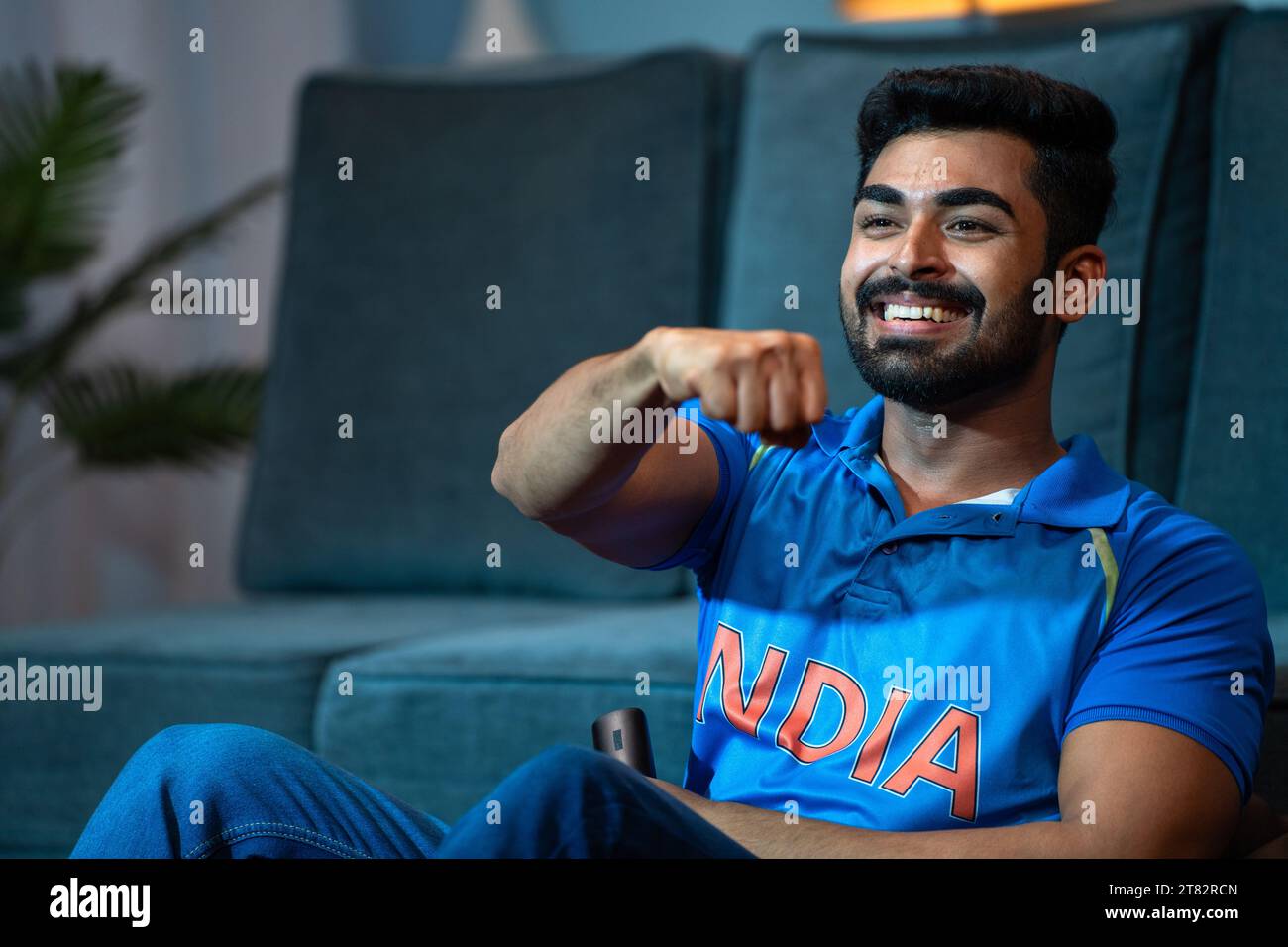 Giovane entusiasta che celebra la vittoria della squadra di cricket indiana mentre guardi la tv a casa: Il concetto di felicità vincente, momenti emotivi e. Foto Stock