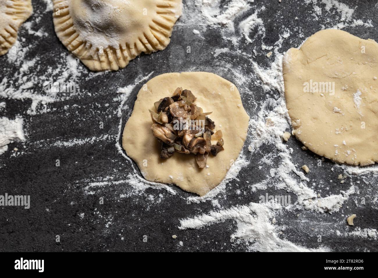 Preparazione di gnocchi senza glutine ripieni di funghi e cipolle. Ripiano grigio scuro cosparso di farina. Fatto in casa. Foto Stock