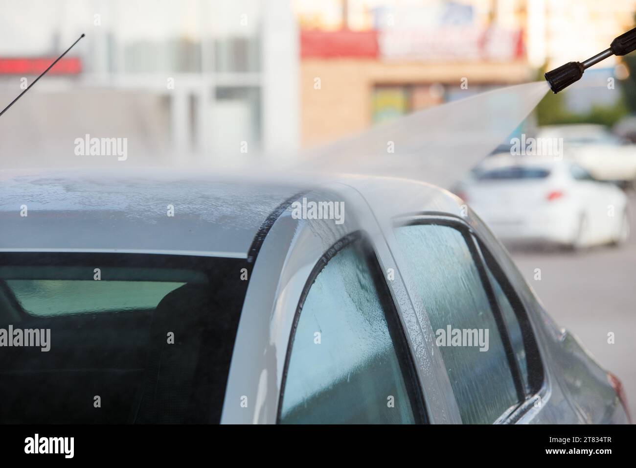 ugello con lavatrice ad alta pressione che spruzza un'auto bianca presso la stazione di lavaggio auto self service pubblica, primo piano con messa a fuoco selettiva Foto Stock