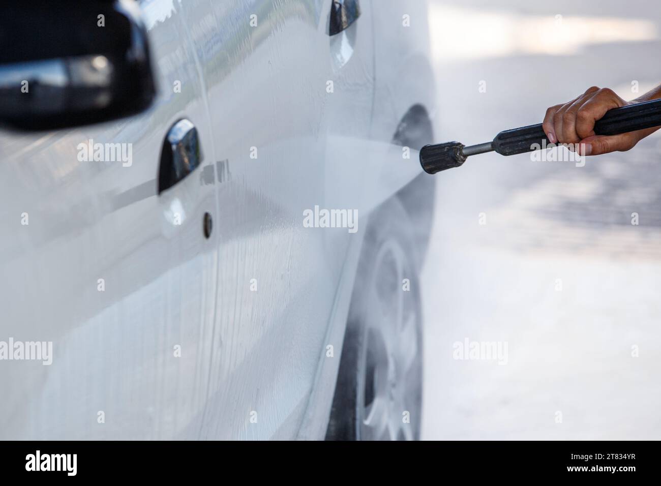 ugello con lavatrice ad alta pressione che spruzza un'auto bianca presso la stazione di lavaggio auto self service pubblica, primo piano con messa a fuoco selettiva Foto Stock