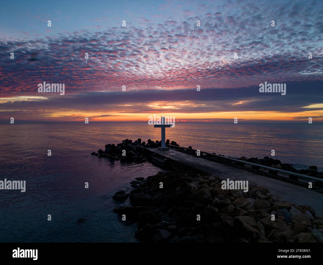 Un volo intorno a una croce cristiana la mattina presto all'alba. La grande croce sorge sul bordo di un frangiflutti sulla costa del mare. Foto Stock