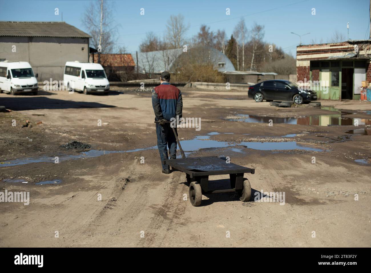 L'uomo tira il carro in fondo alla strada. Il lavoratore sta trasportando un carrello elevatore a forche vuoto. Caricatore al lavoro su strada. Foto Stock