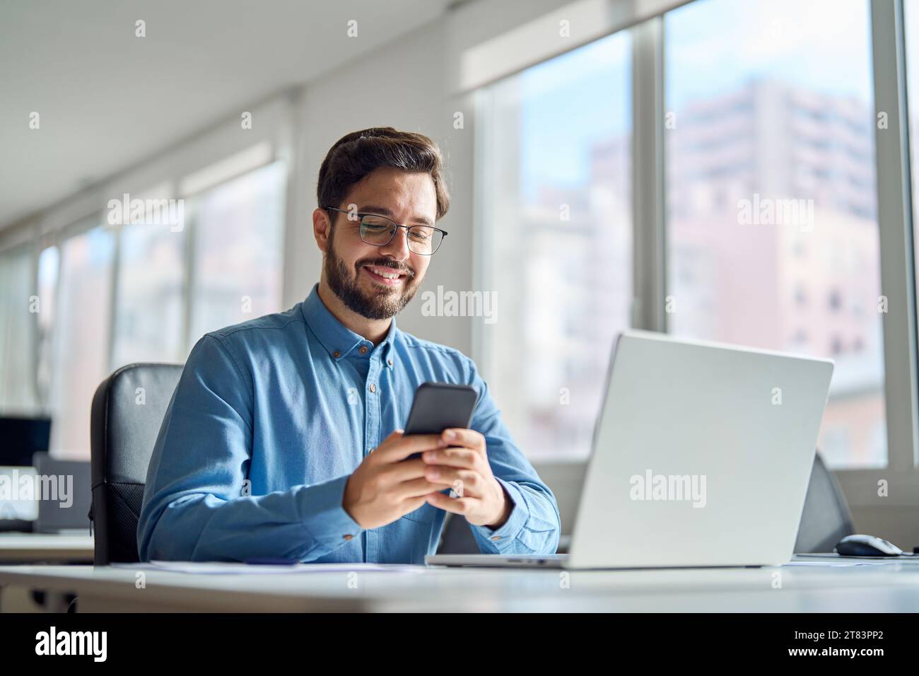 Uomo d'affari latino professionale felice che lavora su un computer portatile utilizzando uno smartphone. Foto Stock