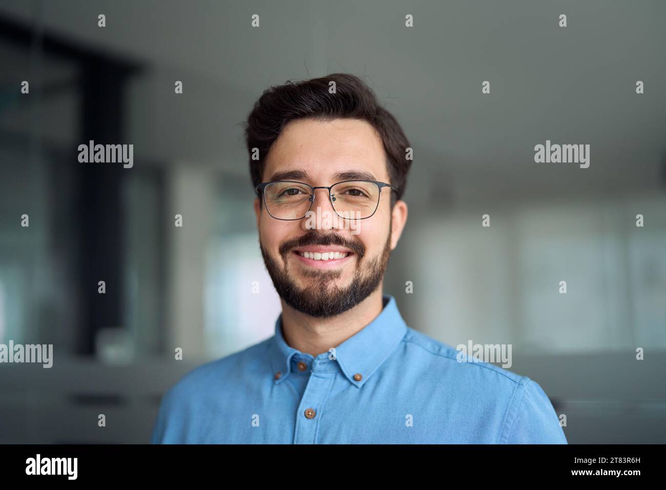 Un giovane uomo d'affari latino sorridente che indossa occhiali, ritratto alla testa. Foto Stock