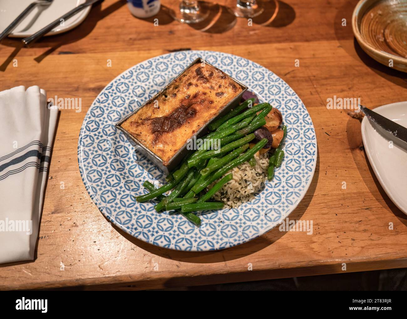 Lasagne al forno con fagioli verdi e riso servite su piatto di ceramica nel ristorante mediterraneo Foto Stock