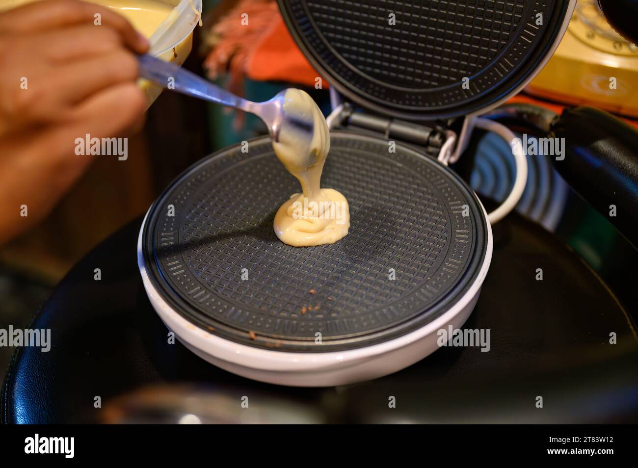 Macchina per la pasticceria dei waffle fatta in casa per preparare e versare l'impasto in padella sulla macchina per teglie in acciaio Foto Stock
