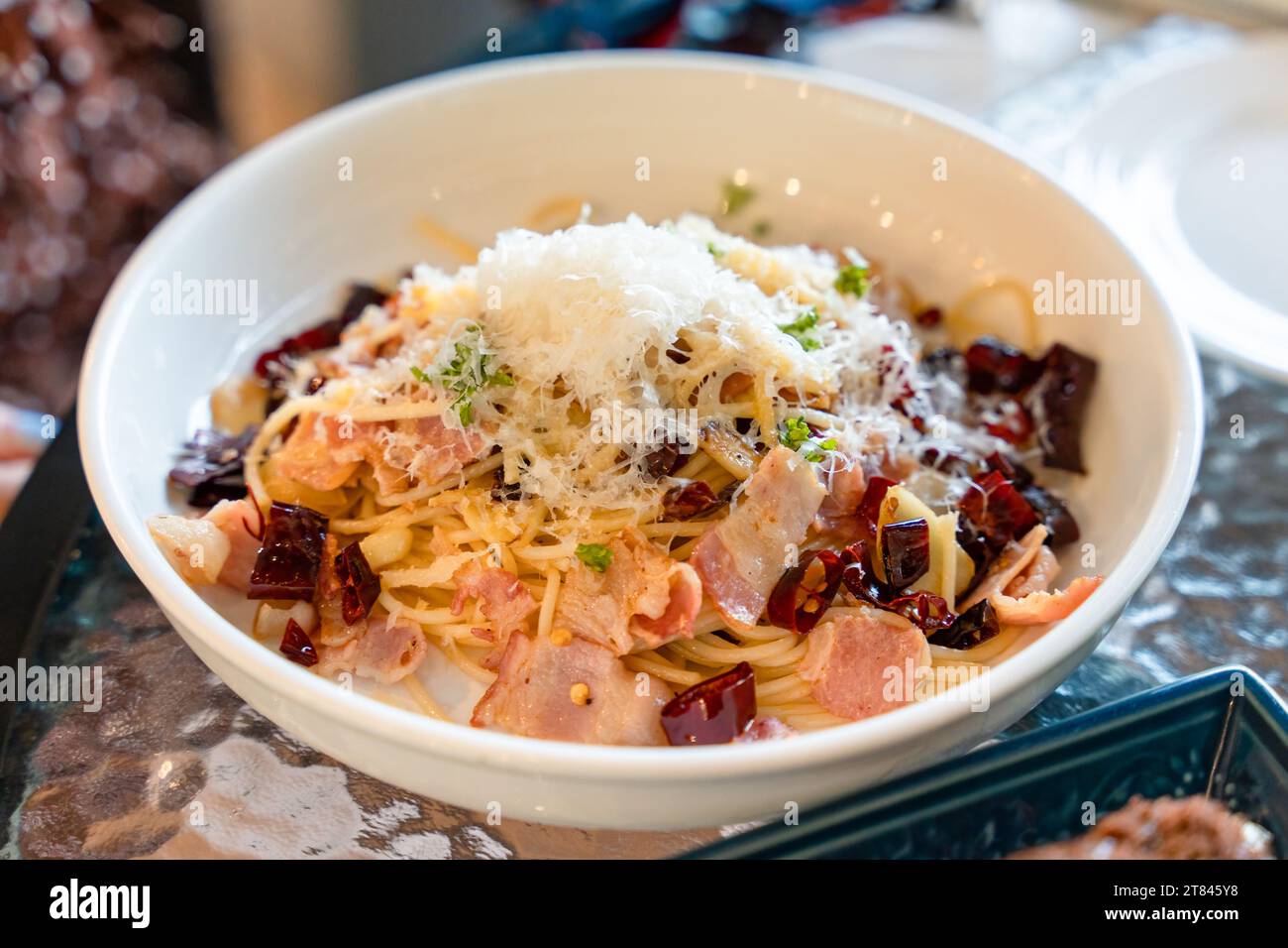 Mescolare il peperoncino secco fritto, la pancetta e le erbe nel piatto bianco del ristorante italiano Foto Stock