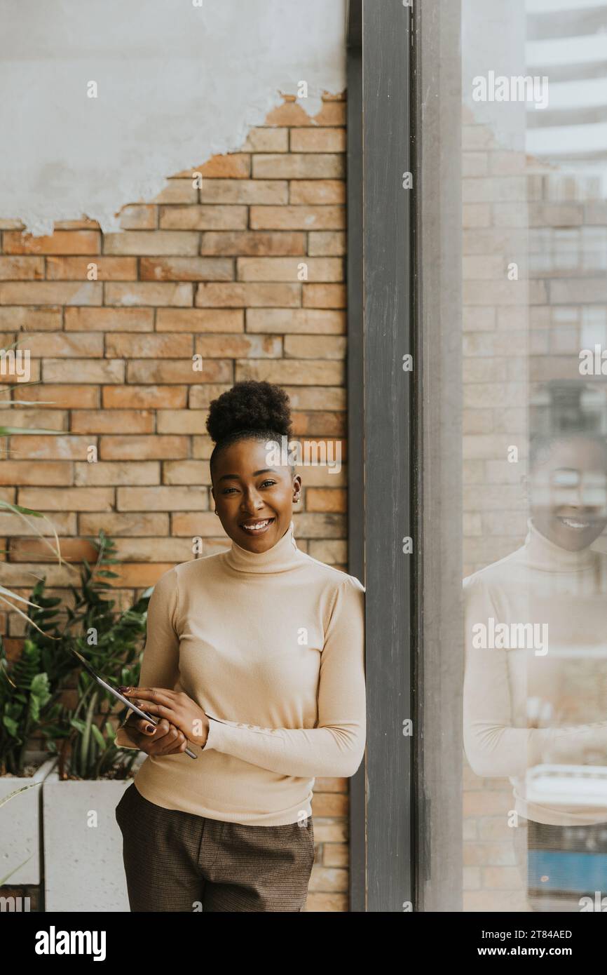 Una bella giovane donna d'affari afroamericana con un tablet digitale in piedi accanto al muro in stile industriale Foto Stock