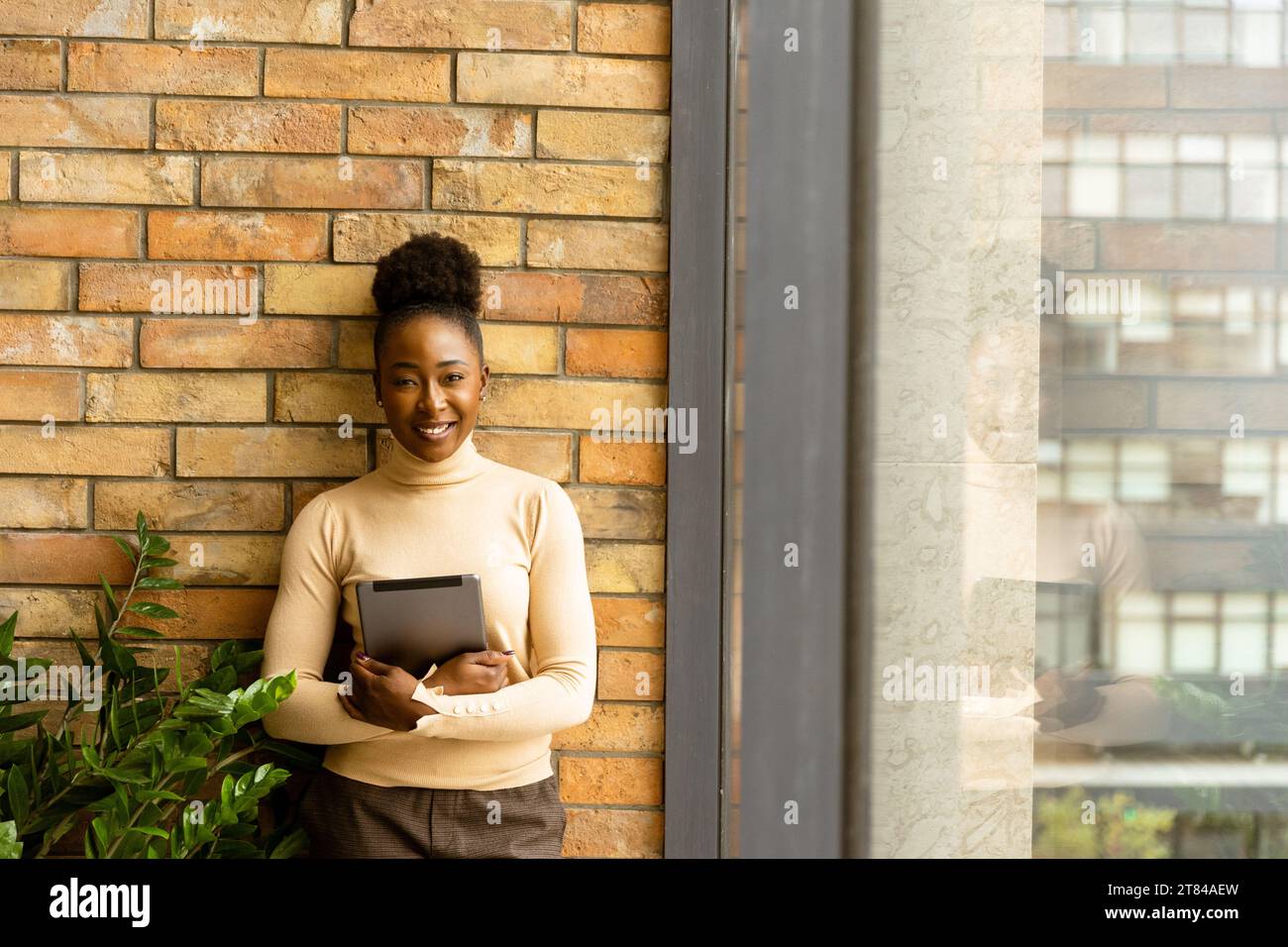 Una bella giovane donna d'affari afroamericana con un tablet digitale in piedi accanto al muro in stile industriale Foto Stock