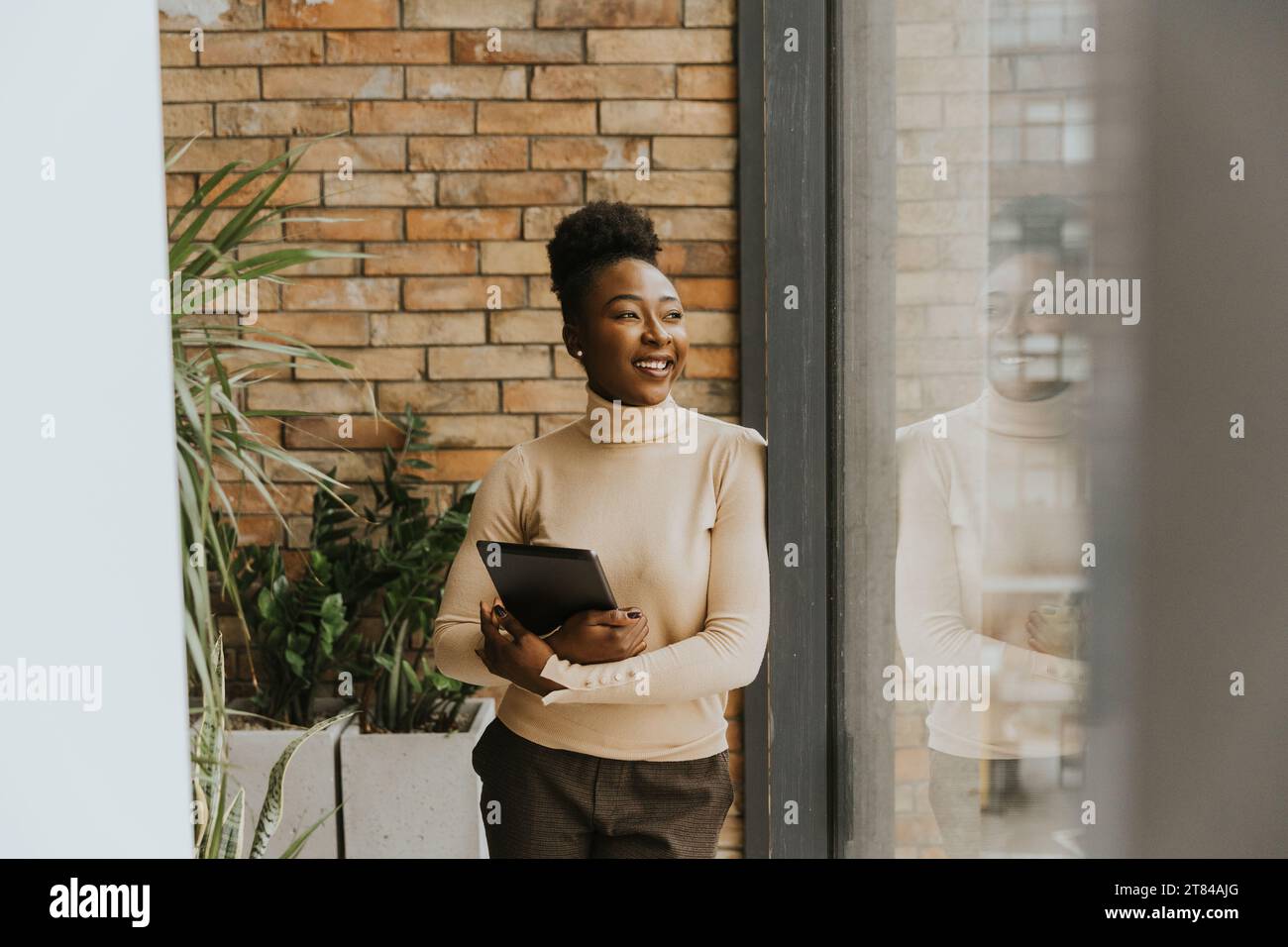 Una bella giovane donna d'affari afroamericana con un tablet digitale in piedi accanto al muro in stile industriale Foto Stock
