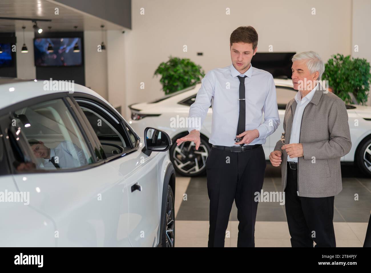 Un venditore mostra un'auto a un uomo anziano in uno showroom. Foto Stock