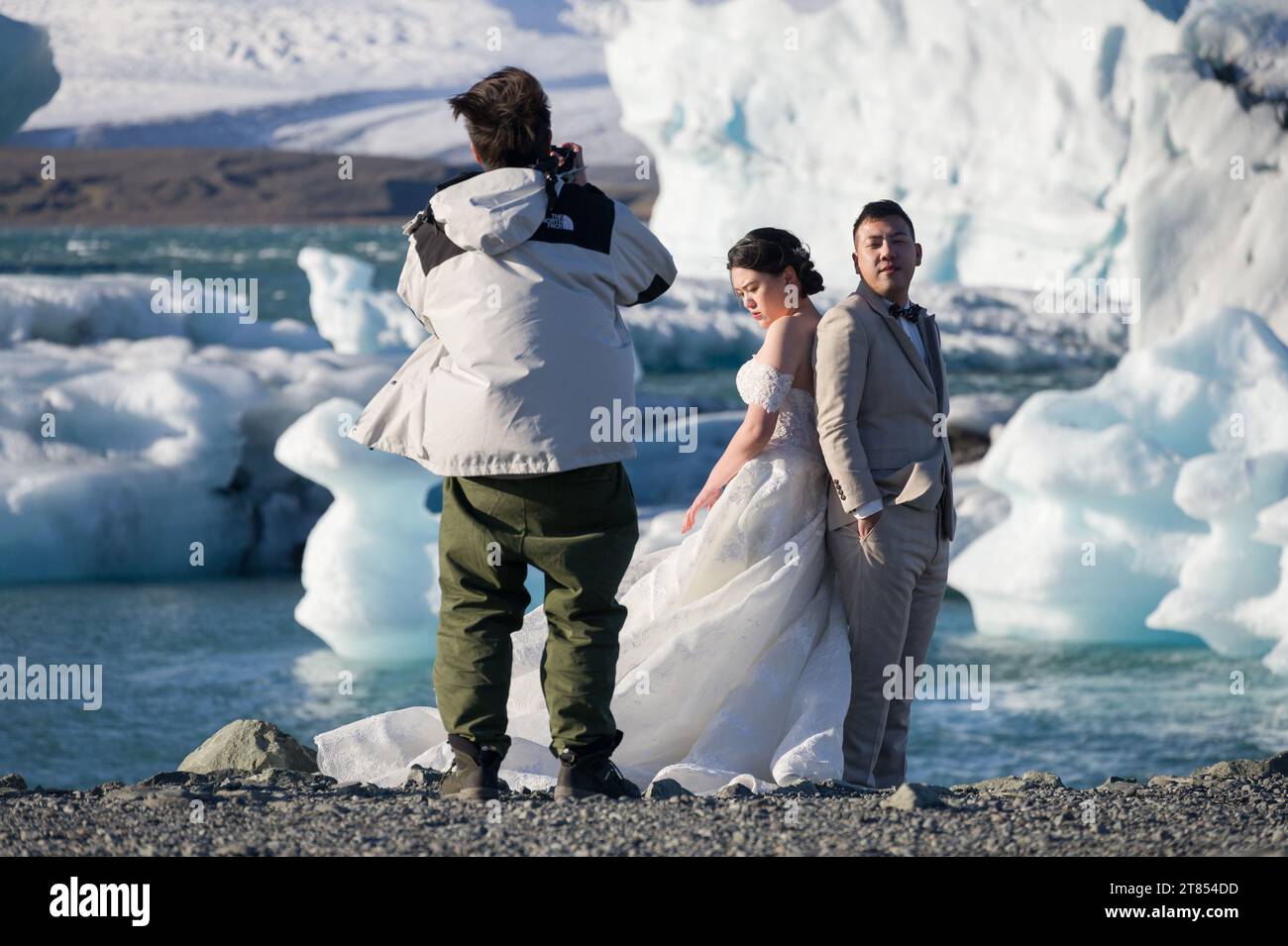 Una coppia asiatica/cinese che indossa un abito da sposa e un abito da sposa posa per foto alla laguna di Jokulsarlon con iceberg sullo sfondo, Islanda Foto Stock