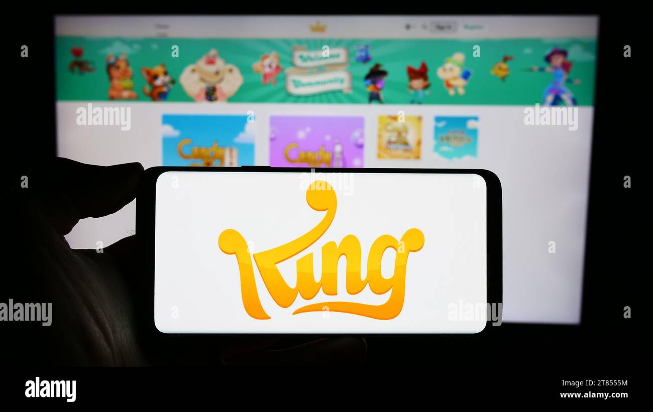 Persona che possiede il cellulare con il logo della società svedese di sviluppo di videogiochi King.com Limited davanti alla pagina Web. Concentrarsi sul display del telefono. Foto Stock