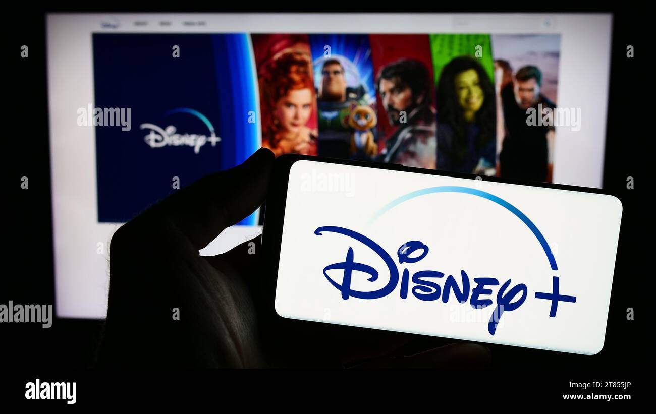 Persona che possiede uno smartphone con il logo del servizio di streaming video on demand degli Stati Uniti Disney Plus davanti al sito Web. Concentrarsi sul display del telefono. Foto Stock