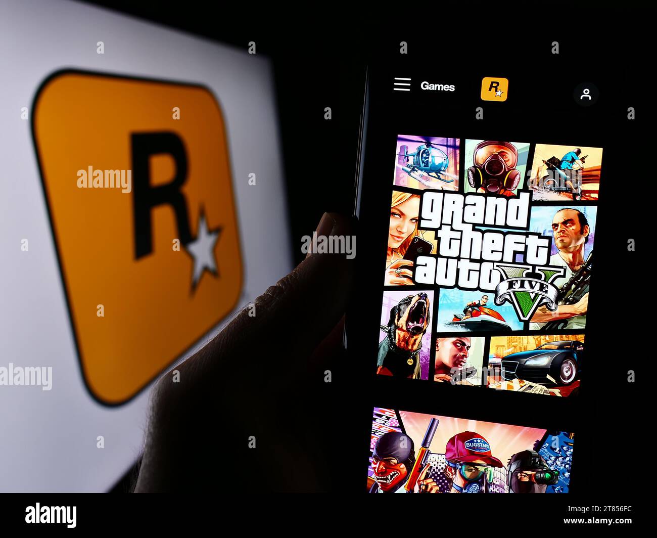 Persona in possesso di cellulare con pagina Web della casa editrice statunitense Rockstar Games Inc. Davanti al logo. Concentrarsi sul centro del display del telefono. Foto Stock