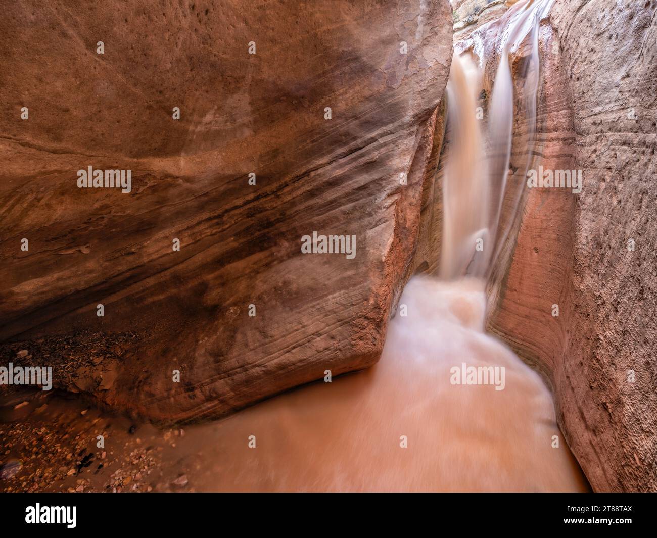 L'acqua fangosa proveniente da Willis Creek scorre attraverso una cascata in una grotta nel Willis Creek slot Canyon, nel Grand Staircase-Escalante National Monument, Utah. Foto Stock