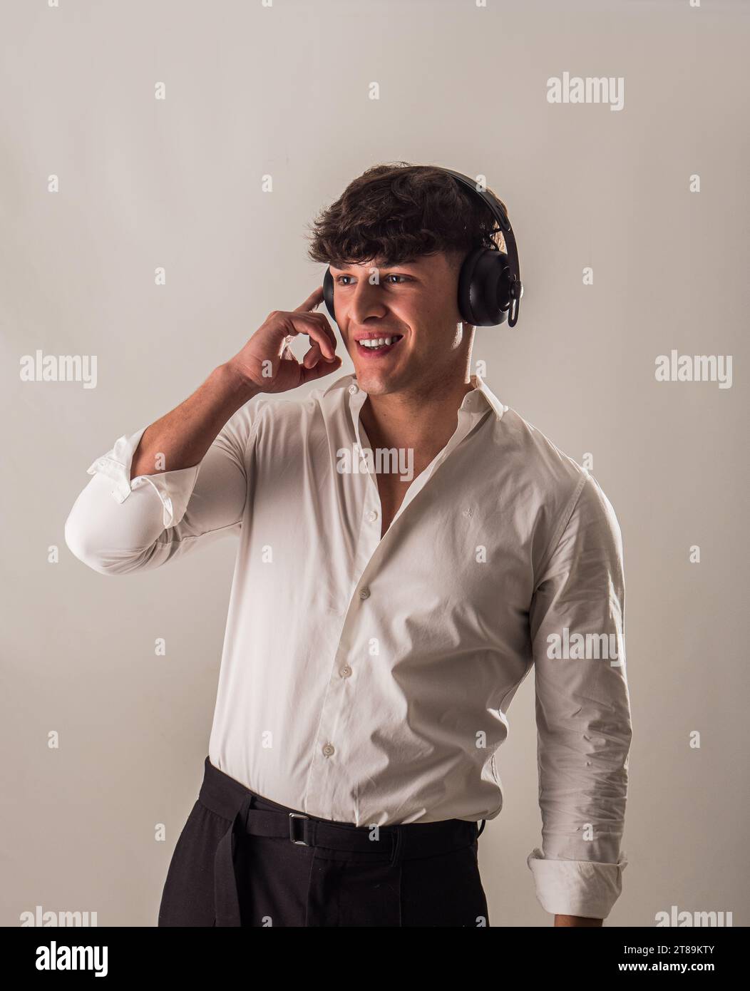 Un giovane e bello uomo con una camicia bianca sta ascoltando musica con le cuffie, in studio Foto Stock
