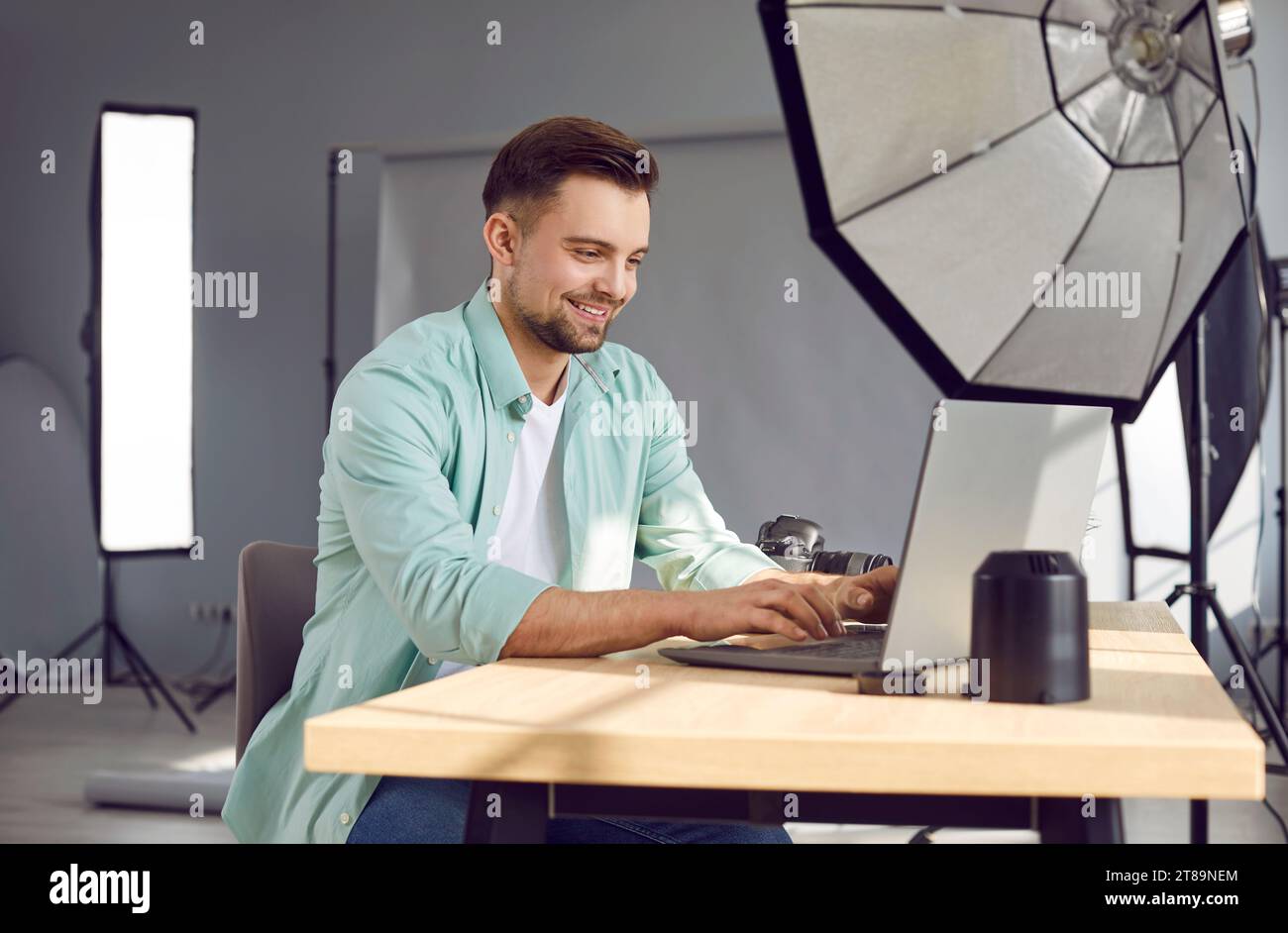Fotografo professionista maschio sorridente che utilizza un computer portatile in uno studio fotografico Foto Stock