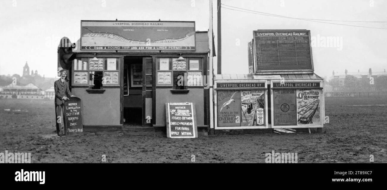 Un ufficio di prenotazione della Liverpool Overhead Railway in una capanna presso un fangoso Aintree Racecourse, Liverpool, Merseyside, Inghilterra, Regno Unito c.1930. Poster e bacheche pubblicizzano i biglietti e i permessi della ferrovia, in particolare per vedere i transatlantici al molo. RMS Scythia, RMS Adriatic e SS Doric sono su un avviso tenuto da un ritaglio di cartone di una guardia ferroviaria (sinistra). Un ramo della ferrovia sopraelevata aprì nel 1906 e servì l'ippodromo per alcuni anni. La ferrovia sopraelevata di Liverpool è stata la prima ferrovia elettrica sopraelevata al mondo. La ferrovia chiuse nel 1956. Foto Stock