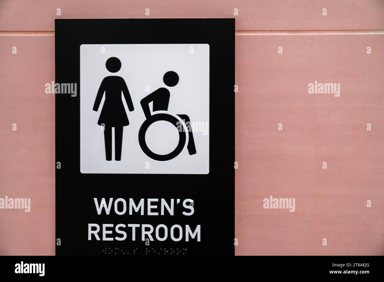 Primo piano del cartello del bagno femminile sulla parete di colore rosa con simboli per la donna e la sedia a rotelle. Copia spazio. Foto Stock