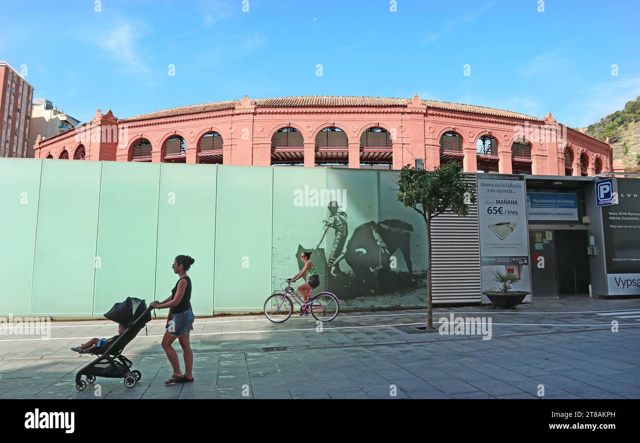 Calle Cervantes Malaga. La famosa arena parzialmente nascosta dietro schermi colorati raffiguranti un matador e un toro. Passa una donna con la carrozzina. Foto Stock