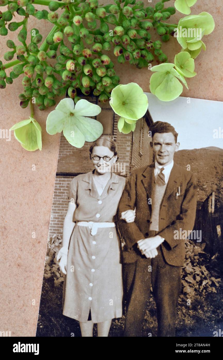 Foto seppia di una giovane coppia sposata degli anni '1930 in piedi fuori dalla loro nuova casa con stelo di fiori di rosa di Guelder adagiato accanto ad essa Foto Stock