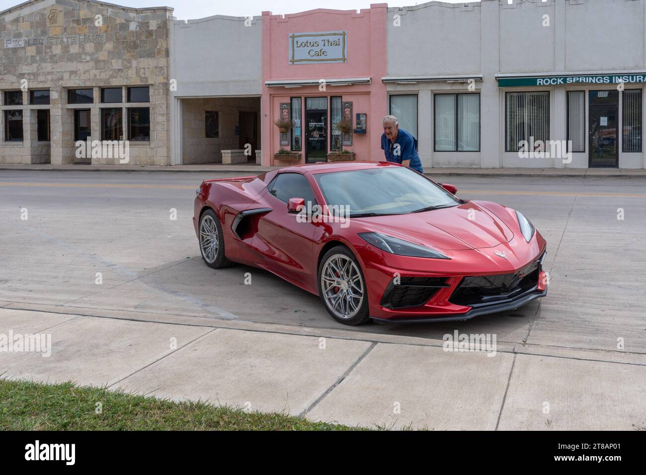 Un uomo anziano sta accanto alla sua corvetta rossa elegante, sportiva e tardiva parcheggiata in strada a Rocksprings, Edwards County, Texas, Stati Uniti. Foto Stock