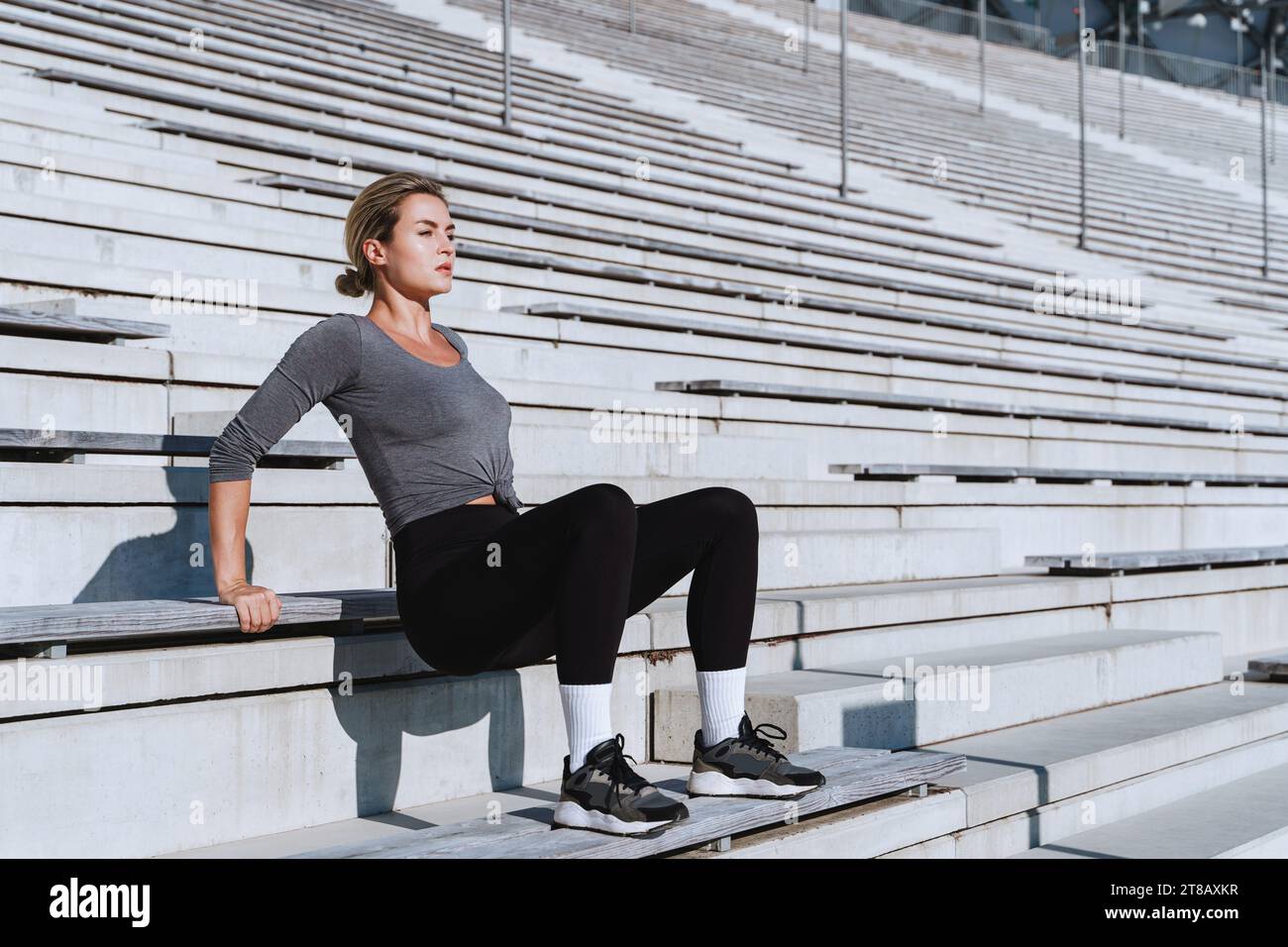 Atleta donna che indossa abbigliamento sportivo femminile che fa triceps tuffi durante l'allenamento calistenico sulle scale dello stadio all'aperto Foto Stock