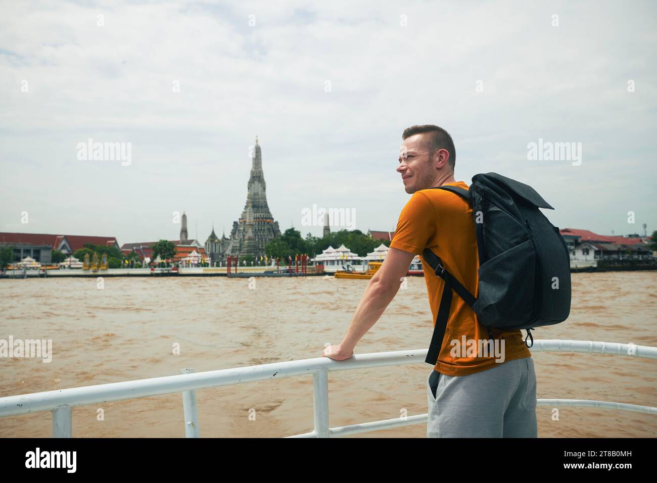 Il viaggiatore con zaino e' godere della vista dal traghetto al tempio Wat Arun a Bangkok. Bellissima destinazione di viaggio in Thailandia. Foto Stock
