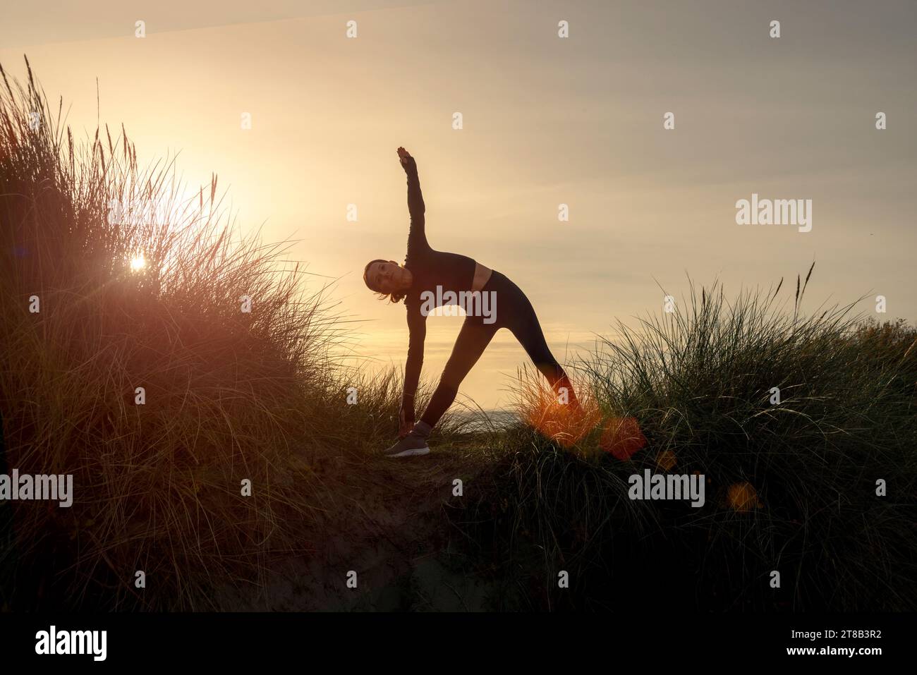 Silhoutte di una donna sportiva che fa una posa da yoga triangolare all'alba Foto Stock