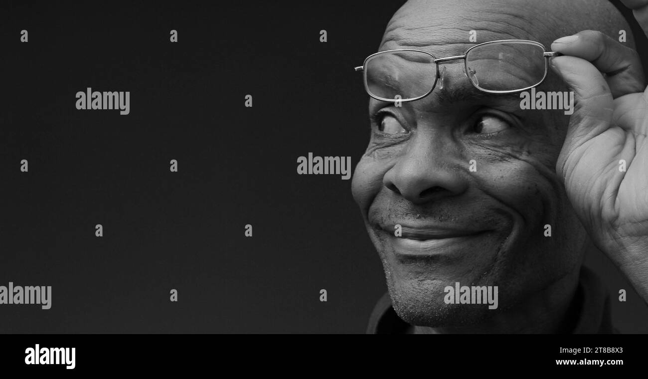 uomo con occhiali da lettura in mano su sfondo grigio con gente che ha una foto in magazzino Foto Stock