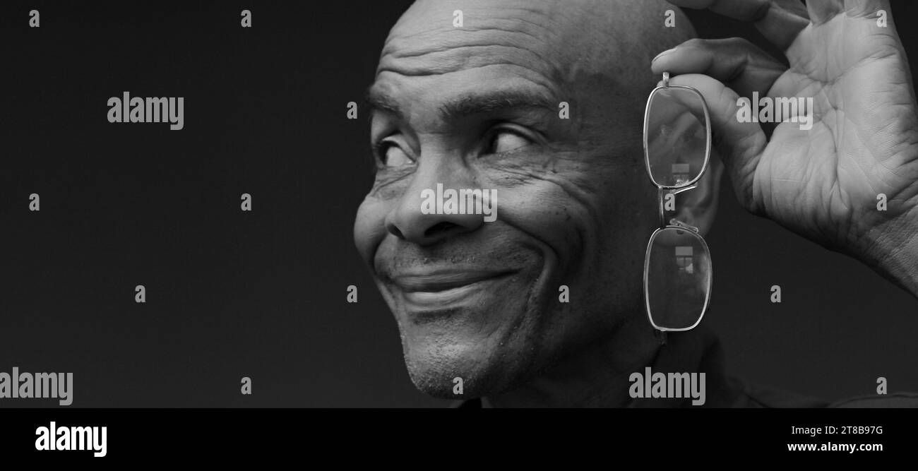 uomo con occhiali da lettura in mano su sfondo grigio con gente che ha una foto in magazzino Foto Stock