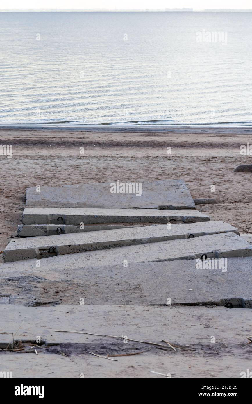 Strada di cemento rotta che attraversa la spiaggia fino alla costa del Golfo di Finlandia Foto Stock