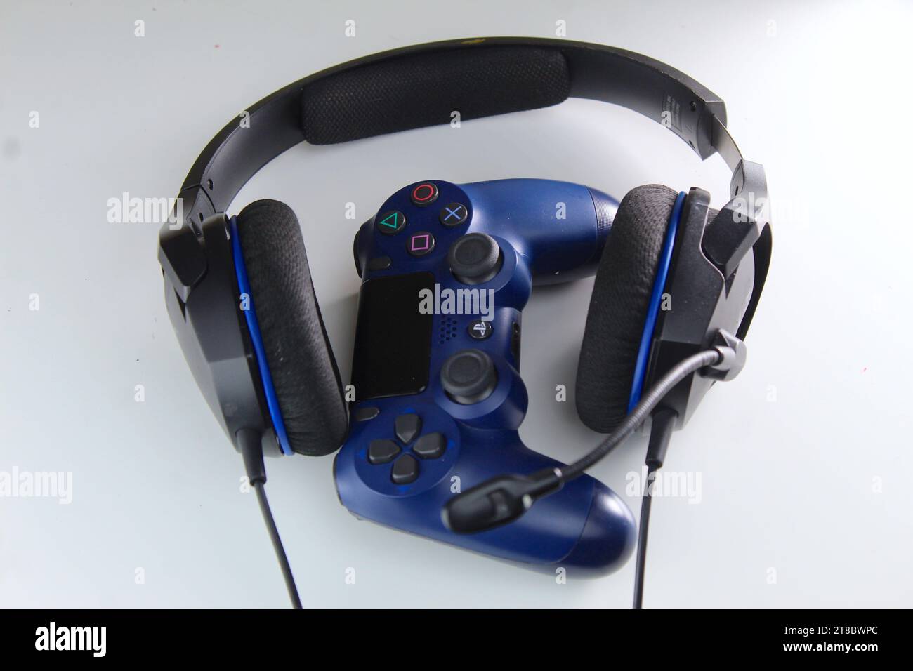 Una foto di un controller console di gioco PlayStation blu scuro e un paio di cuffie su un tavolo bianco. Videogamer. Foto Stock