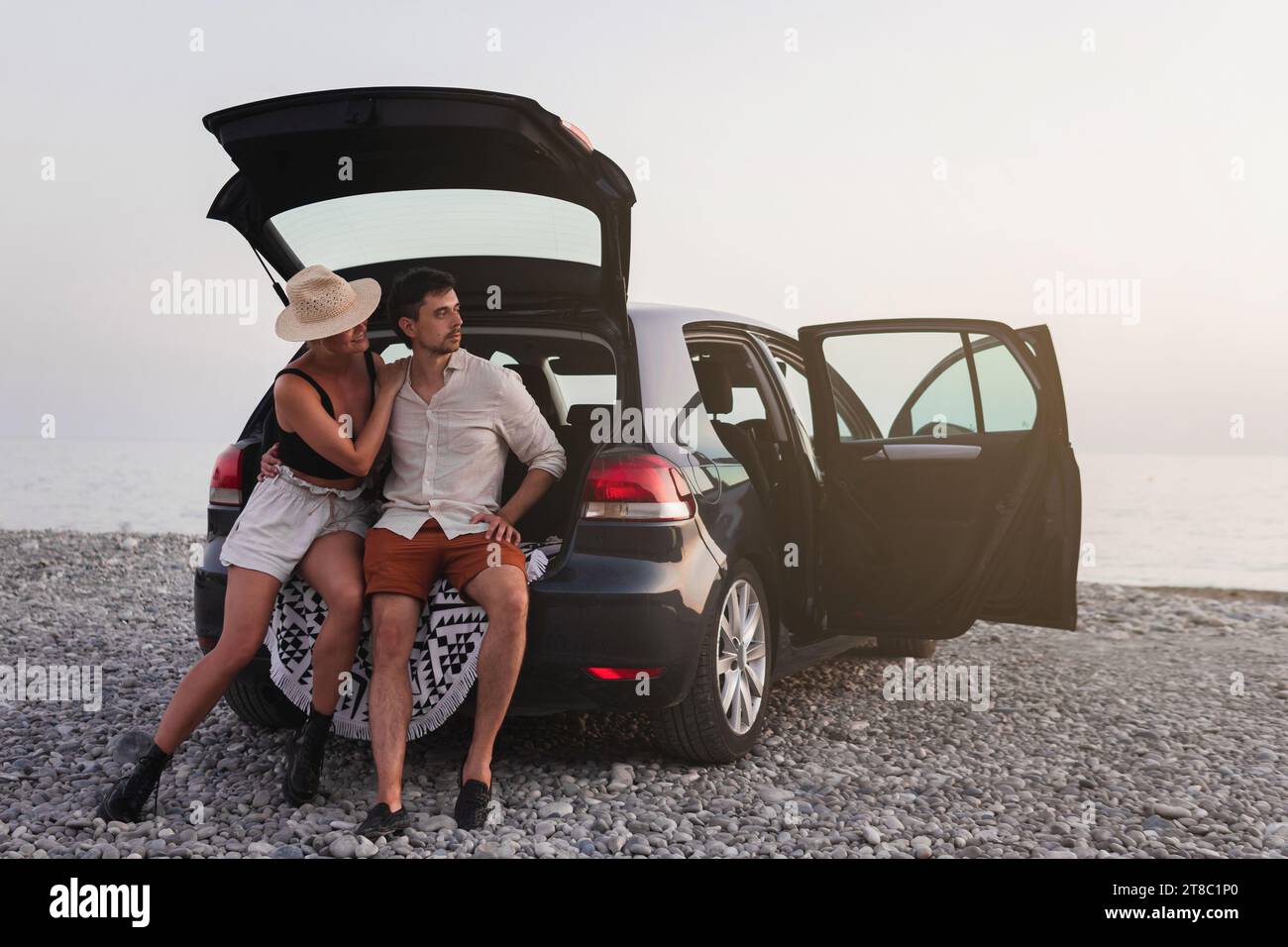 Un paio di viaggiatori in piedi accanto alla loro auto su una spiaggia di ciottoli durante il loro viaggio in auto Foto Stock